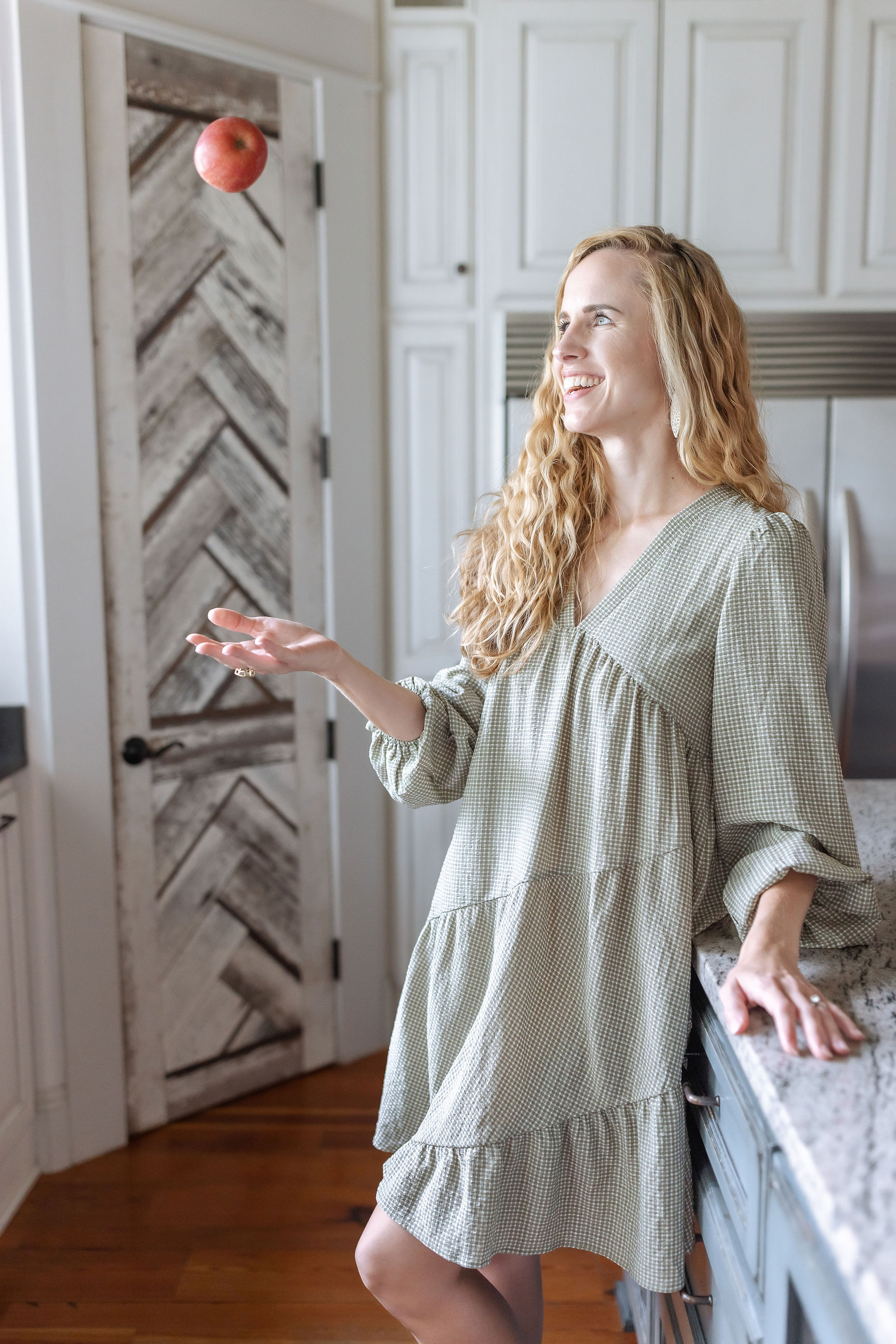 Woman tossing an apple to catch it in white and grey kitchen to show how you can stop feeling out of control with food