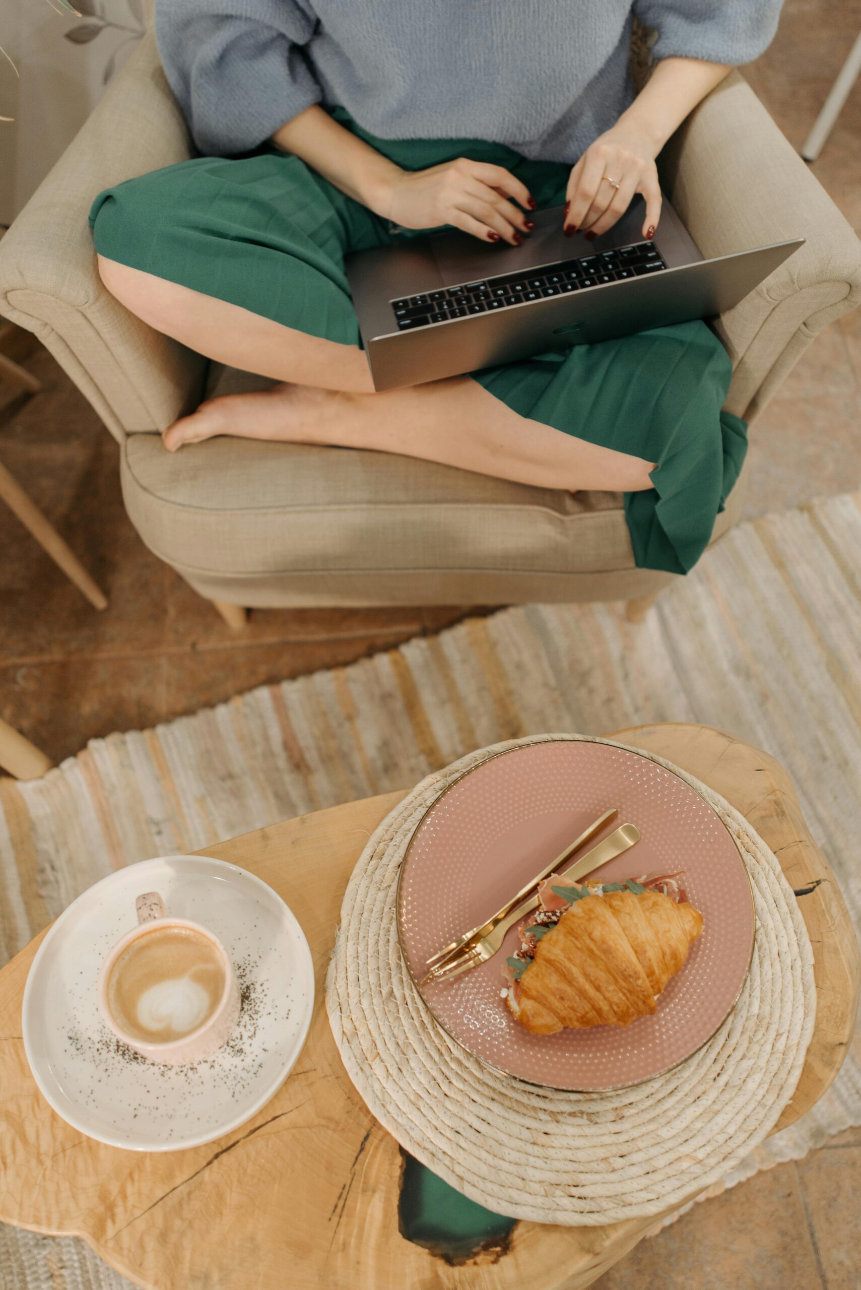 Woman sitting on chair using laptop with coffee and croissant counseling for eating disorder recovery